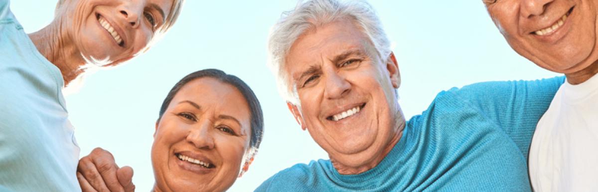 Four older adults with greying hair, arms around each other's shoulders, smiling at the camera