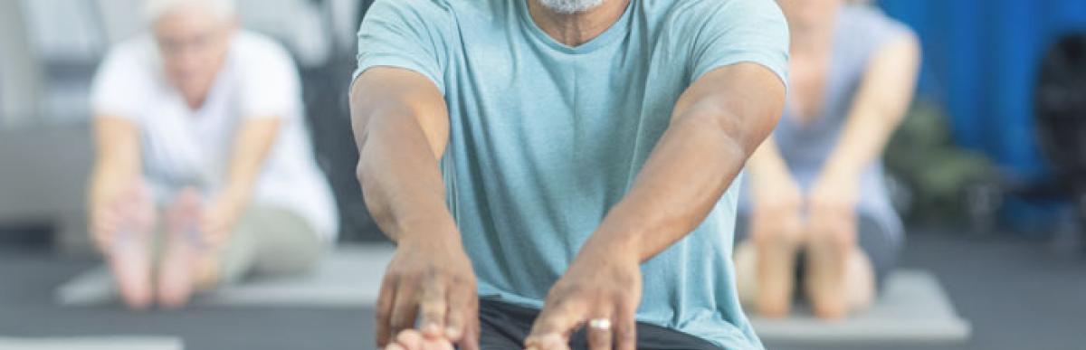 Older man smiling at camera while stretching on a yoga mat