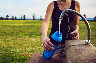 Woman filling up a water bottle at an outdoor tap