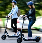 Tow women riding e-scooters on the street wearing helmets