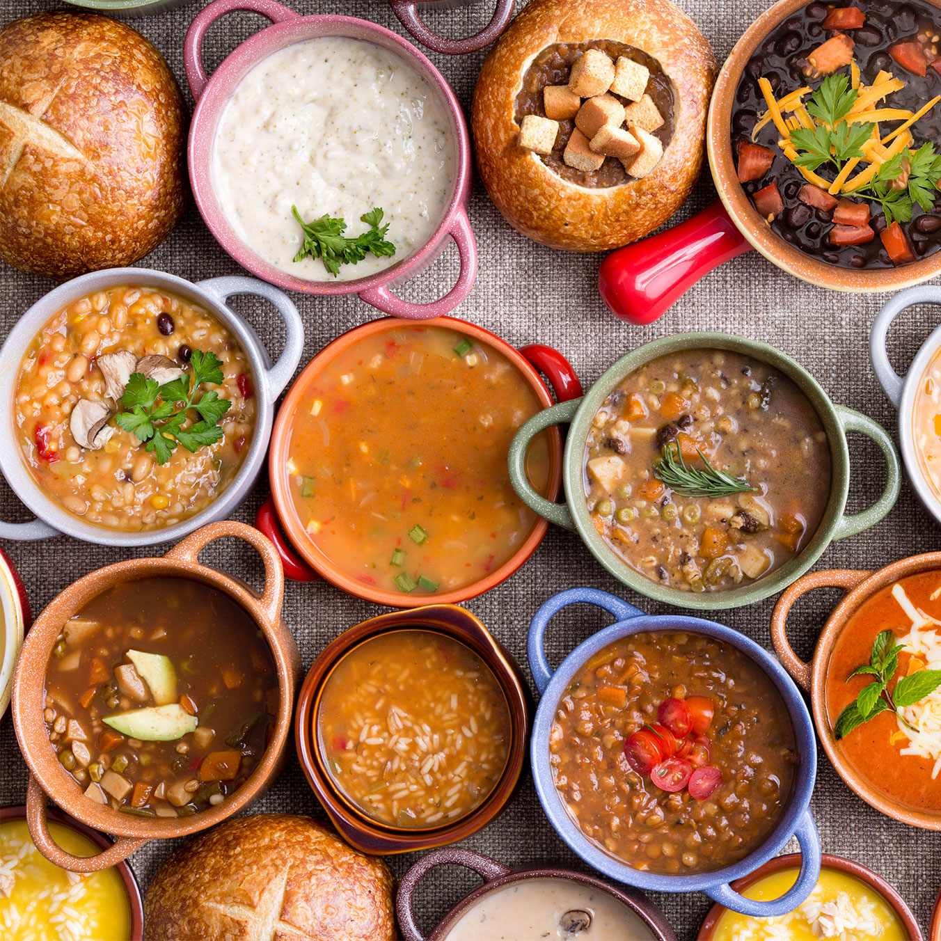 top view of various bowls of soups and stews in ceramic and bread bowls