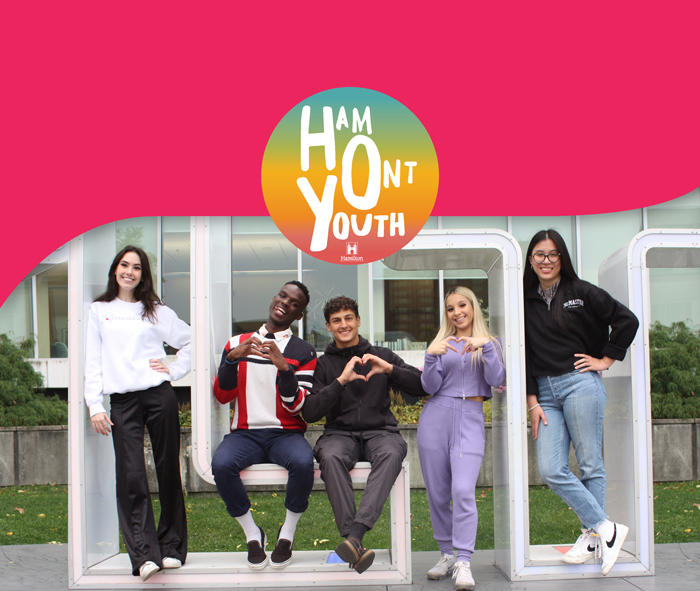 5 young adults sitting on Hamilton Sign at City Hall