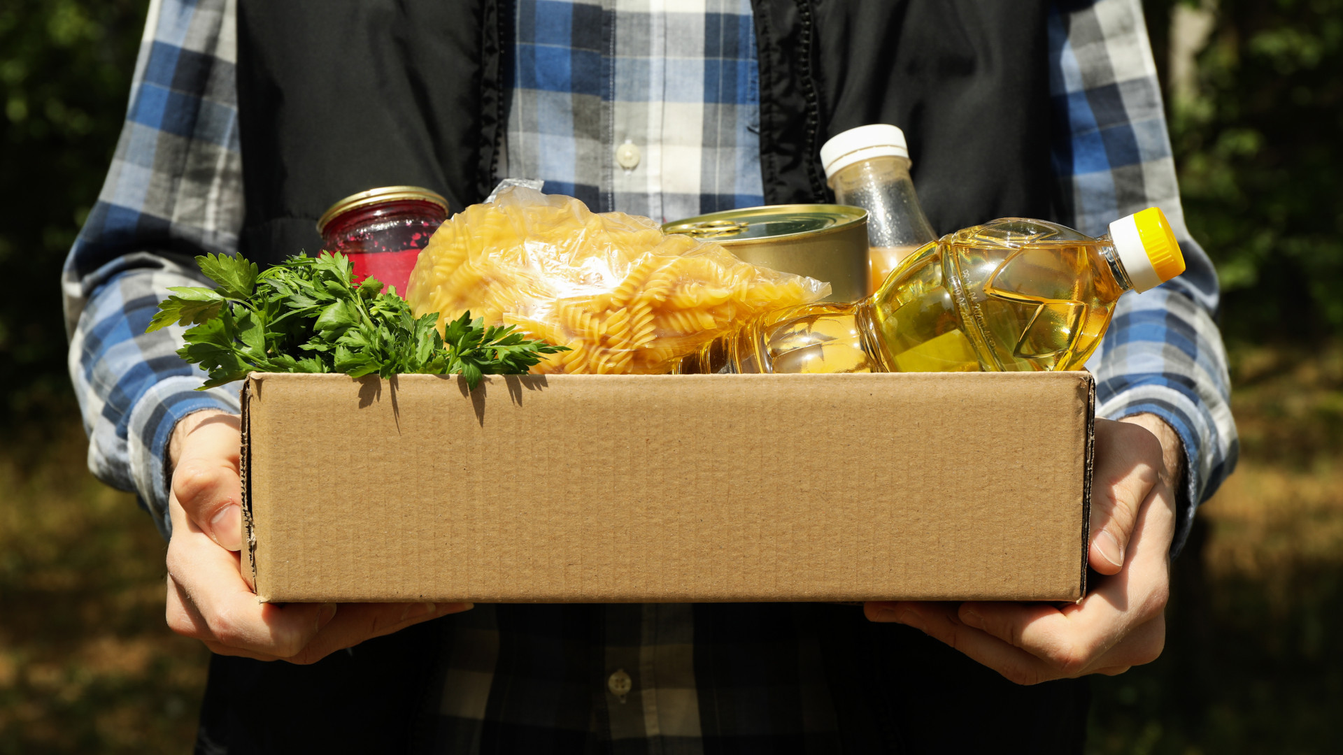 Person holding a box of food, pasta, oil, vegetables