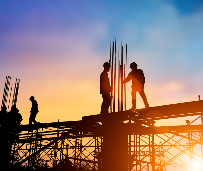 construction workers standing on rafters with a setting un in the background