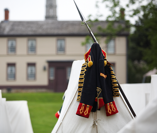 A historical costume jacket and bayonet lean against a tent on the lawn on Battlefield Park museum