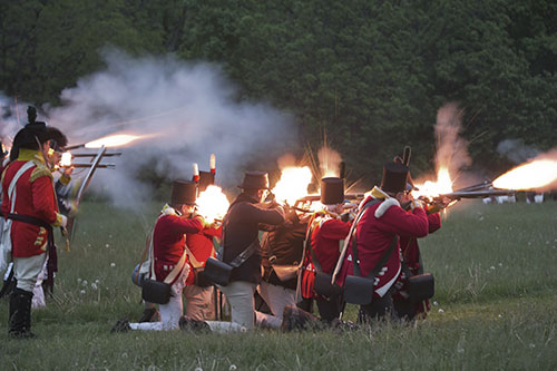 Re-enactment of costumed soldiers firing prop weapons in a field