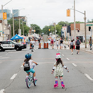 Two children biking and rollarblading towards the closed street for Open Streets event in June 2024