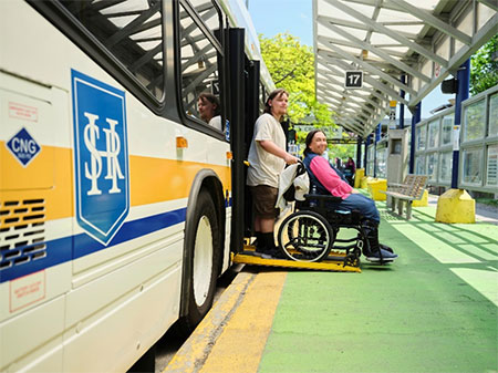 Person in a wheelchair exiting an HSR bus via the rear doors, assisted by another person.