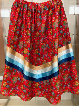 Indigenous ribbon skirt, flowered red with beige, white, blue and light blue ribbons along the bottom