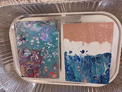 Aluminum pan with two pour paint canvases resting in it. 