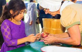 A woman in period costume demonstrated an apple peeler for a child.