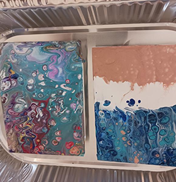 Aluminum pan with two pour paint canvases resting in it. 