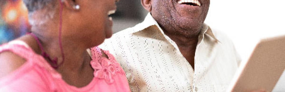 Older man and woman holding a tablet and laughing