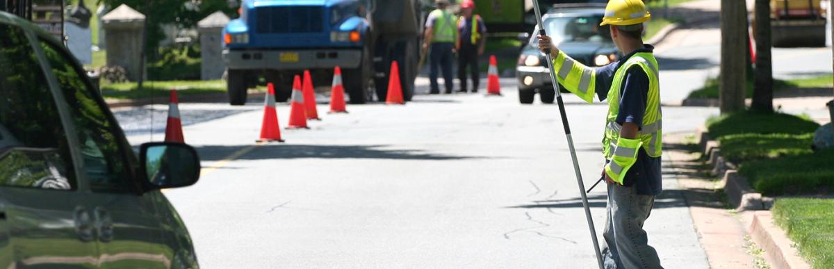 Road construction in neighbourhood with construction worker holding Stop Sign to control traffic