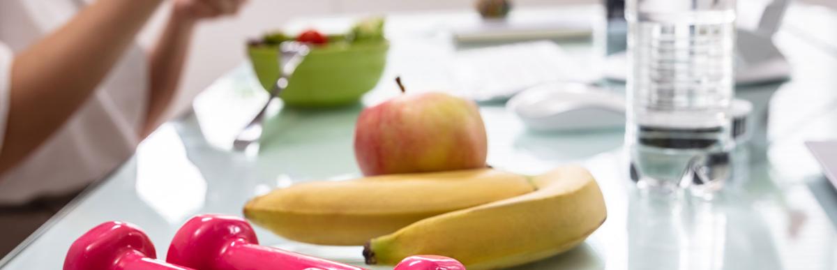 Employee in office eating healthy food, drinking water with small weights on her desk.