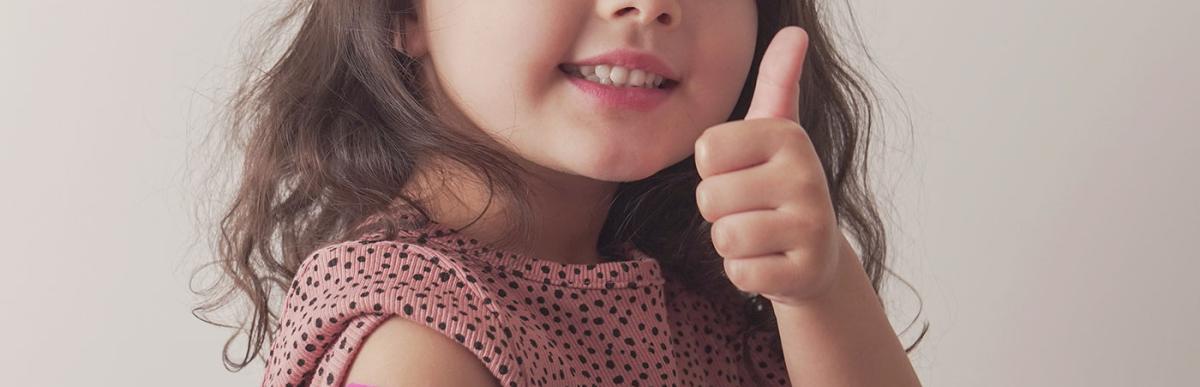 Young mixed Asian girl giving thumb up and showing her arm with pink bandage after got vaccinated or inoculation.