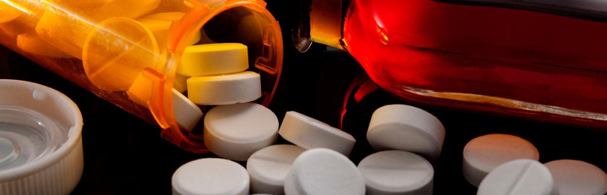 Pills fallen out of a prescription pill bottle next to a flask of hard liquor.