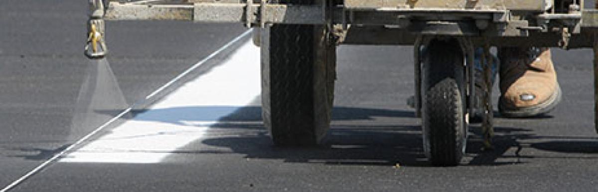 Worker and machine painting white line on road