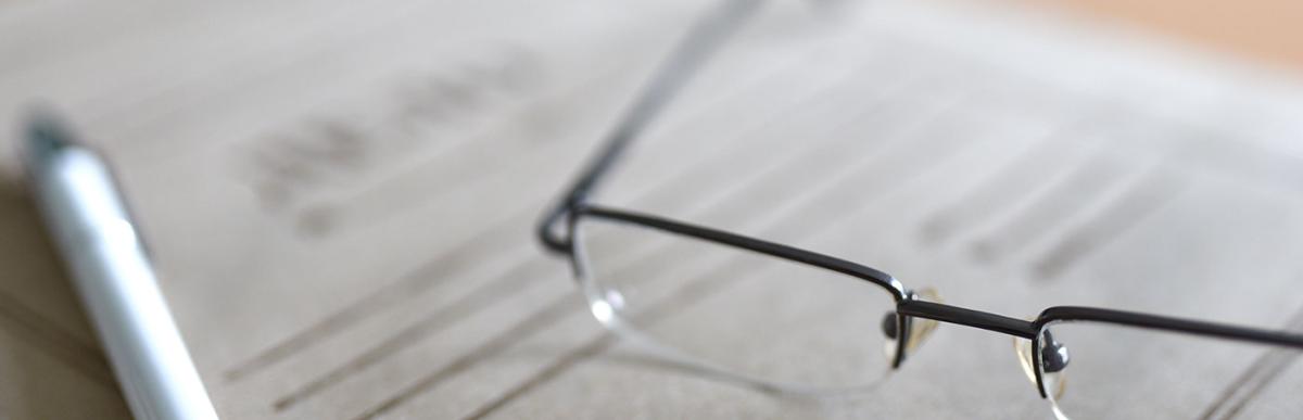 Paper folder with documents on the table, glasses, pen.