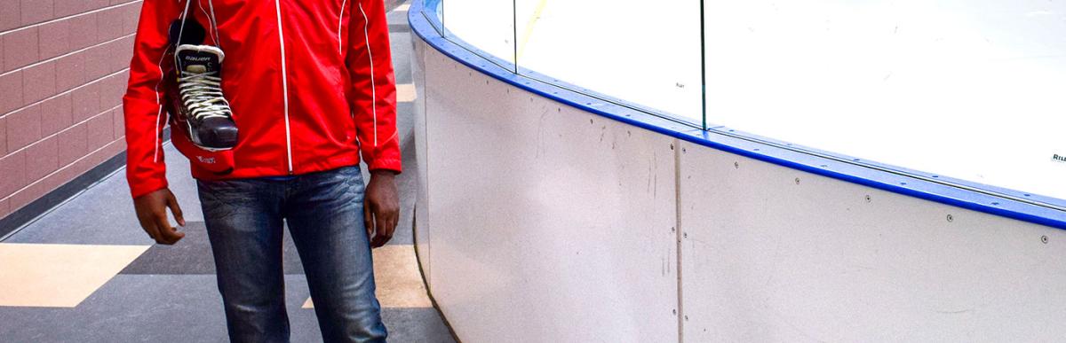 Man wearing Hamilton work jacket with a pair of ice skate over his shoulder at an arena