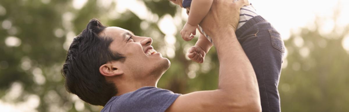 Father holding baby in the air with trees in the background.