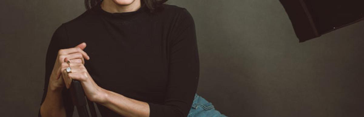 Photo of woman with long brown hair and a black shirt, sitting in a chair