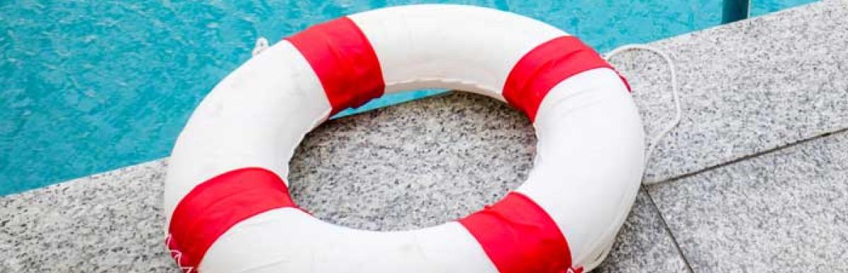 A lifeguard's rescue ring sitting on the edge of an in ground pool.