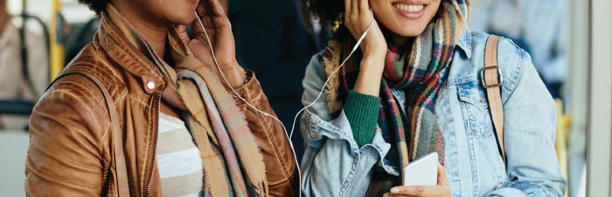 2 women on a bus sharing headphones