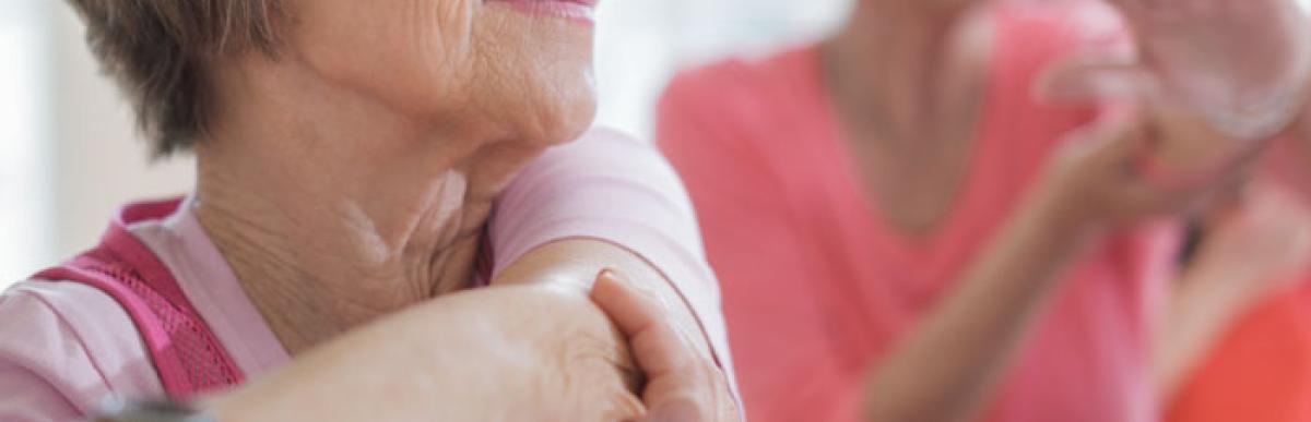 Two older women stretching their arms across their chests in a fitness class