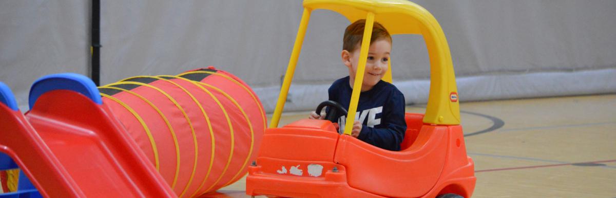 Smiling child sitting in a play car inside a recreation centre gym