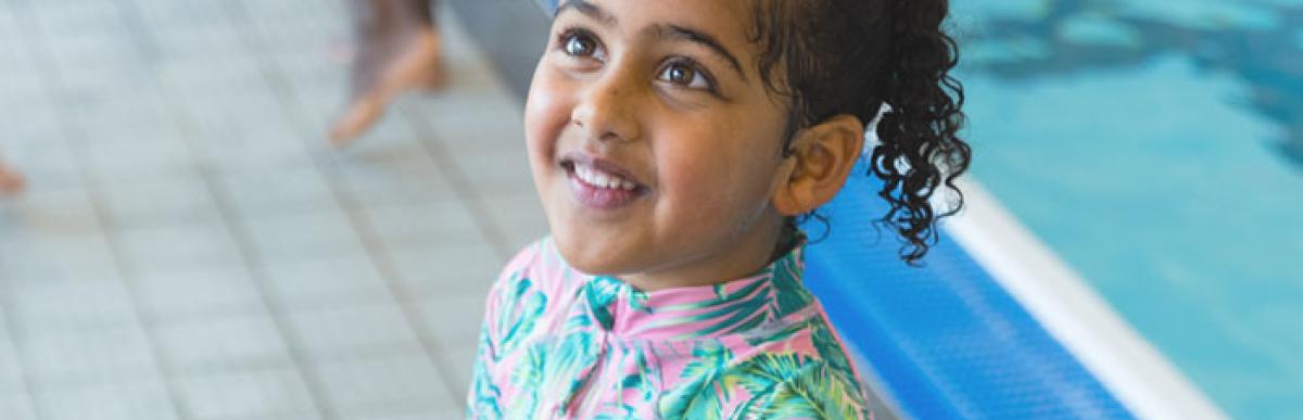 A smiling child standing beside an indoor swimming pool