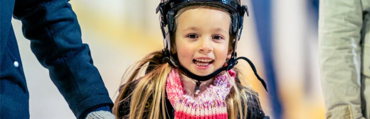 Little girl ice skating and holding her parents hands