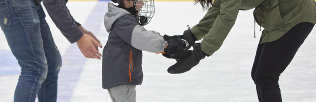 Man and woman assisting a child in skating at an indoor arena