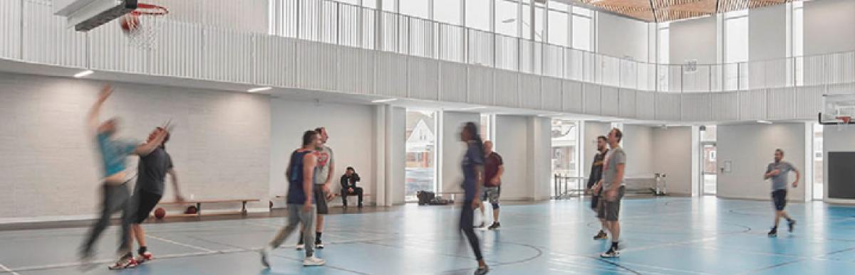 Interior of Bernie Morelli Recreation Centre gym, with a group of people in motion playing basketball.