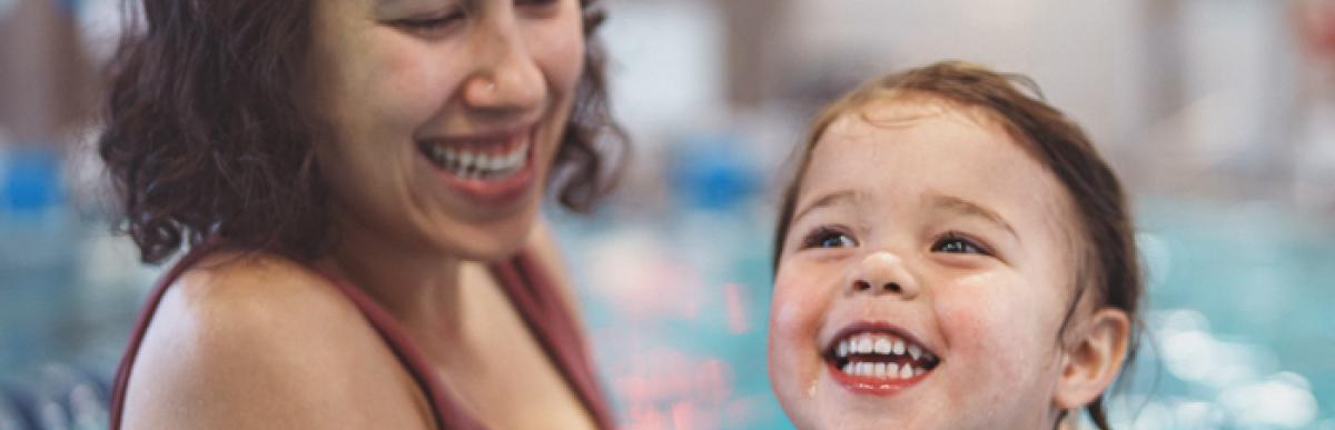 Woman holds a child wearing water wings in an indoor swimming pool