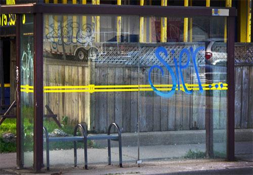 Image of a bus shelter with spray paint graffiti on the glass wall