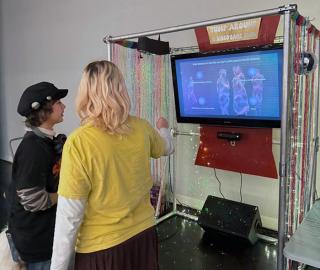 2 people looking at a tv monitor decorated with coloured fabric, lights and a disco ball